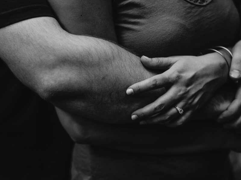 A man hugs a woman from behind in black and white.