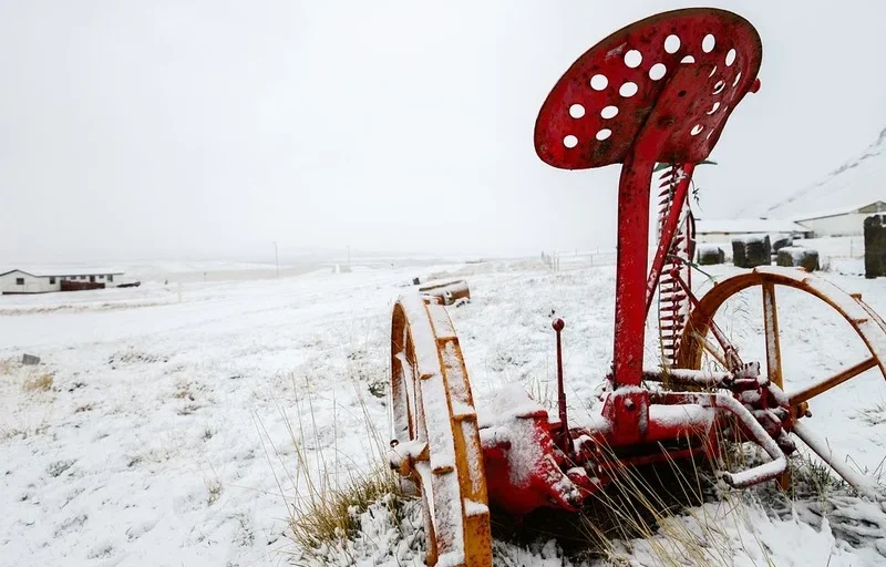 An antique piece of farm equipment in the snow in winter.