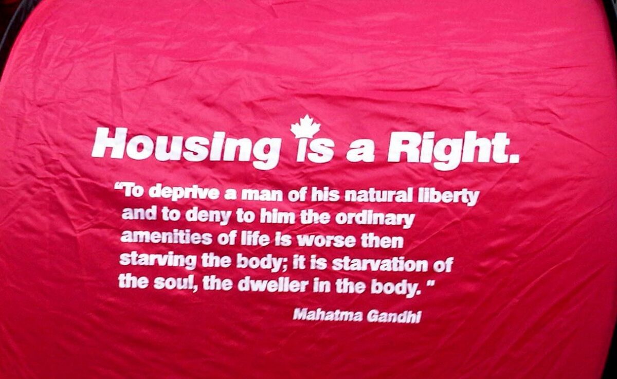 A quote by Mahatma Ghandi about housing being a human right on a red canvas.