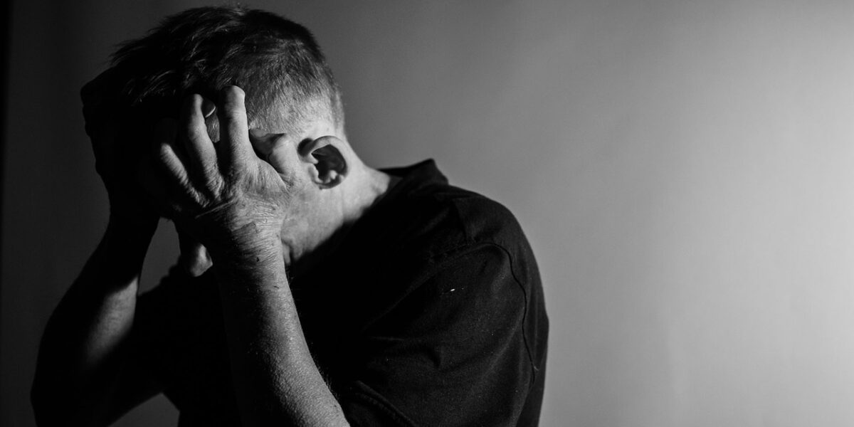 A man holds his head in his hands in a black and white photo.