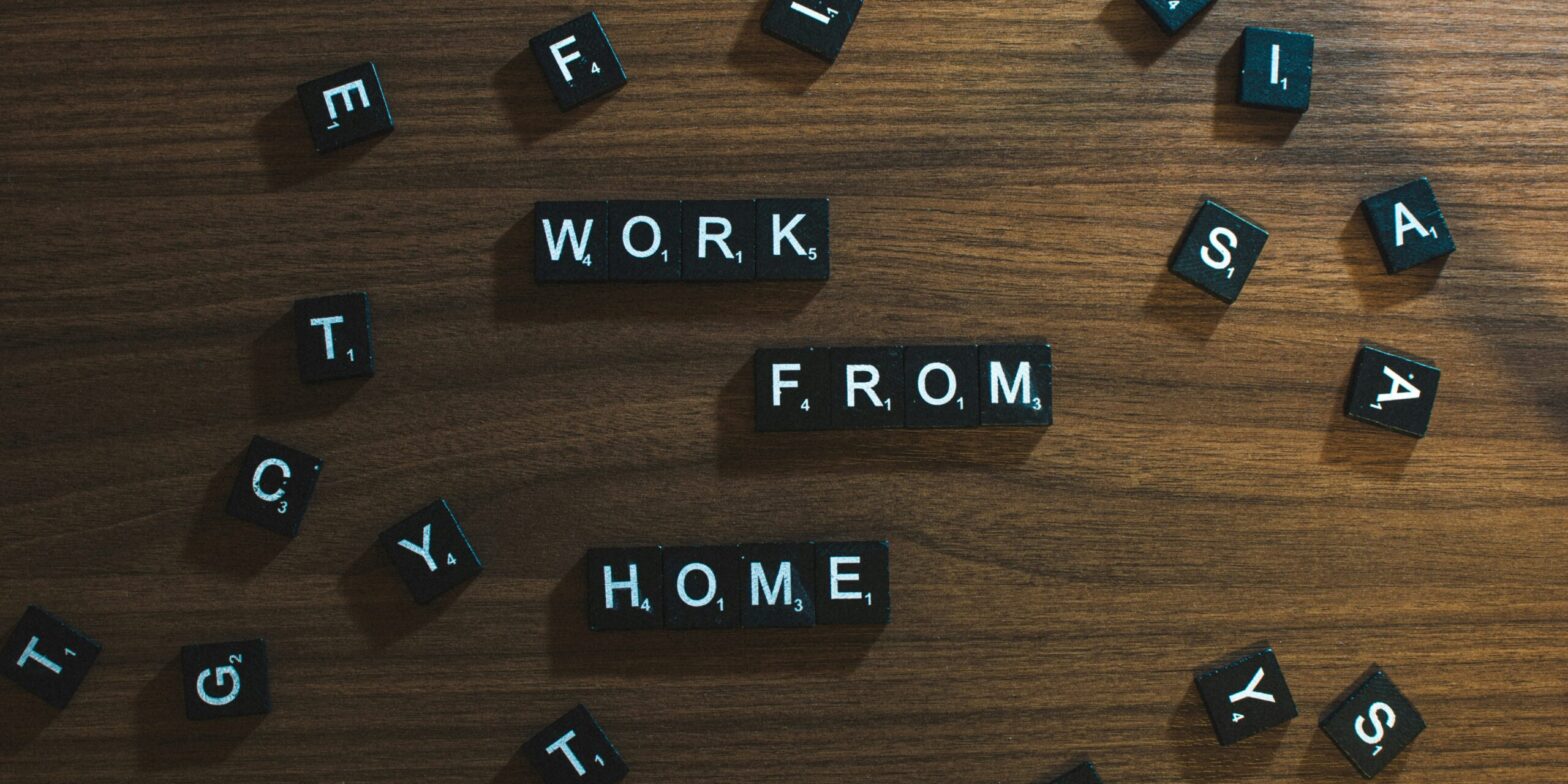 An image of scrabble tiles scattered on a wooden table. The tiles are arranged to say, "Work from home."