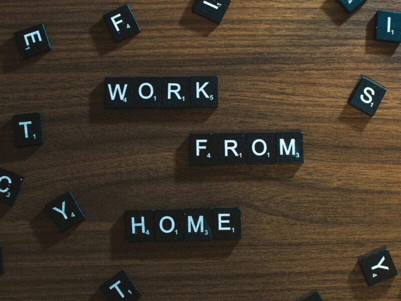 An image of scrabble tiles scattered on a wooden table. The tiles are arranged to say, "Work from home."