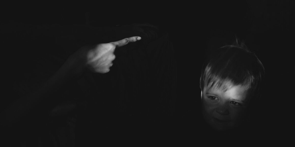 A black and white photo of a finger pointing at a child in shadow.