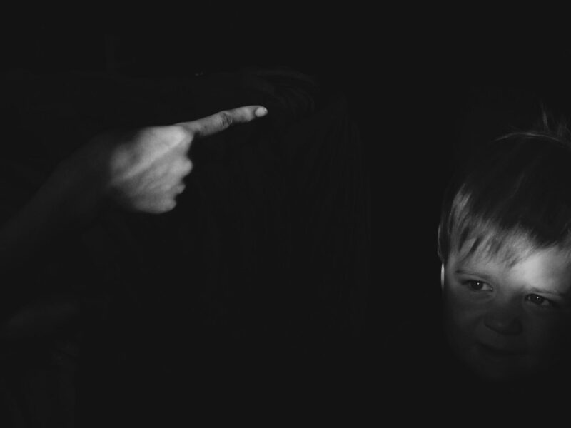 A black and white photo of a finger pointing at a child in shadow.