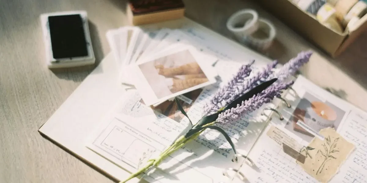 Some lavender, polaroids and stamps scattered over the open page of a journal. Junk journaling gives people somewhere to put all their sentimental mementos.