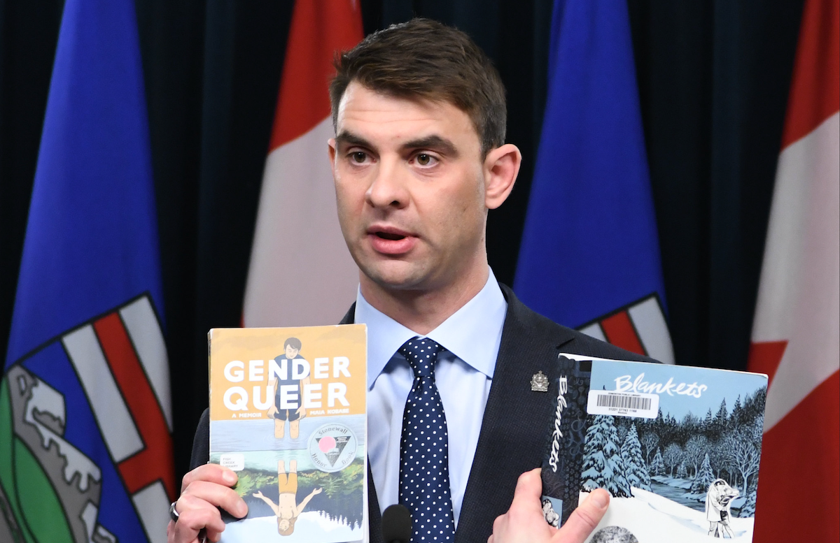 Municipal Affairs Minister Dan Williams holding up a pair of graphic novels on LGBTQ+ themes at the centre of his MAGA-style culture wars campaign.
