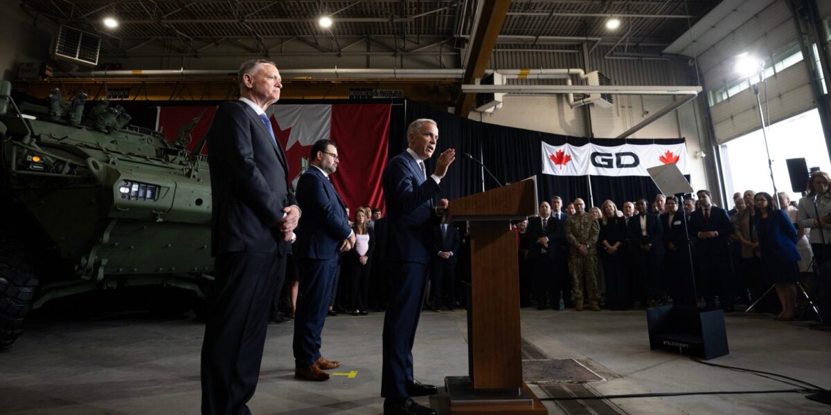 Prime Minister Mark Carney giving a speech in front of a military vehicle.