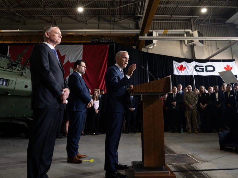 Prime Minister Mark Carney giving a speech in front of a military vehicle.
