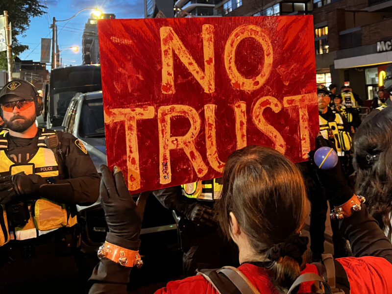 A protester holds up a sign reading "No Trust" during a demonstration against Mark Carney's conference with oligarchs where parts of Canada's public infrastructure was up for sale.